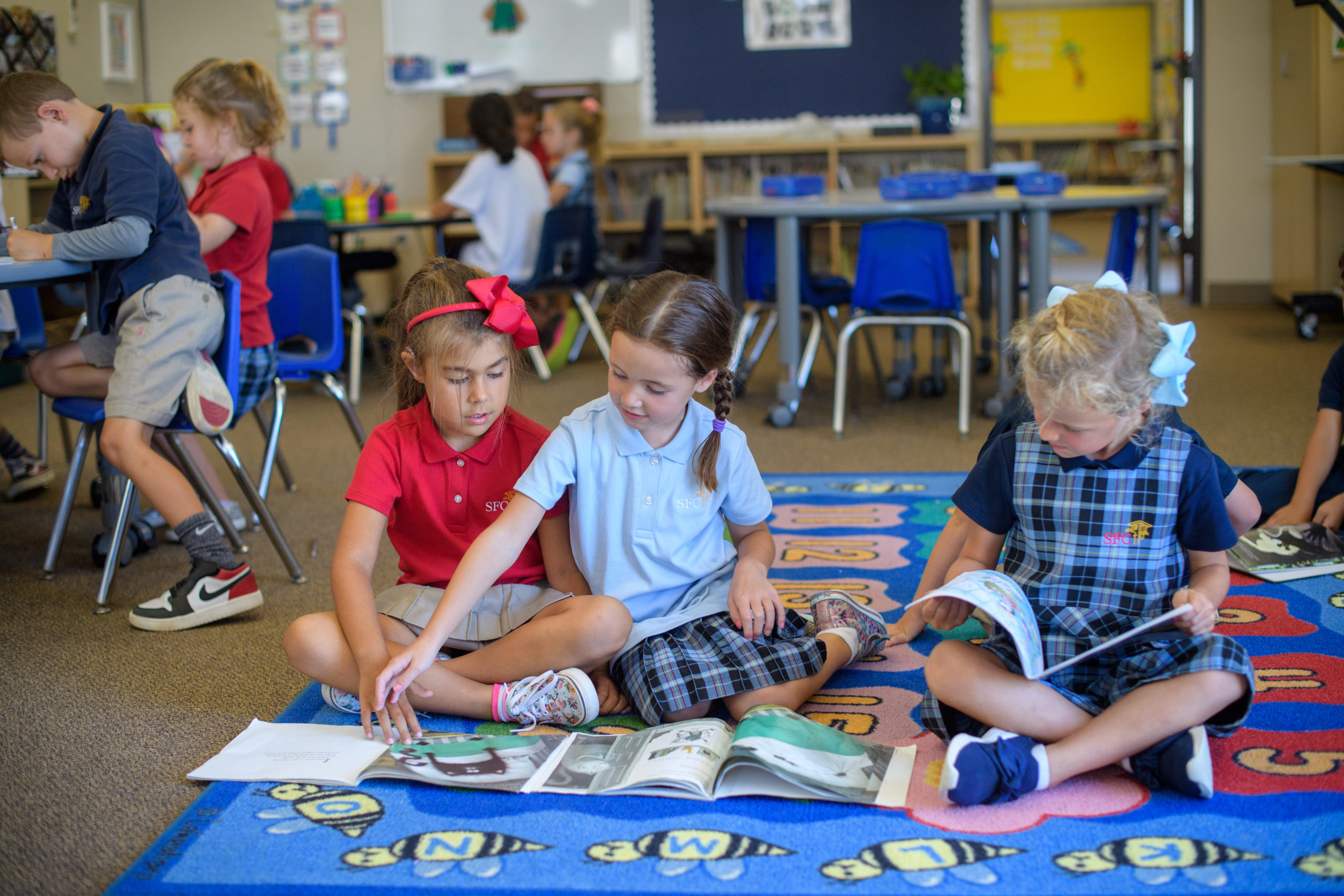 Three Santa Fe Christian kindergarteners reading books on a colorful carpet.