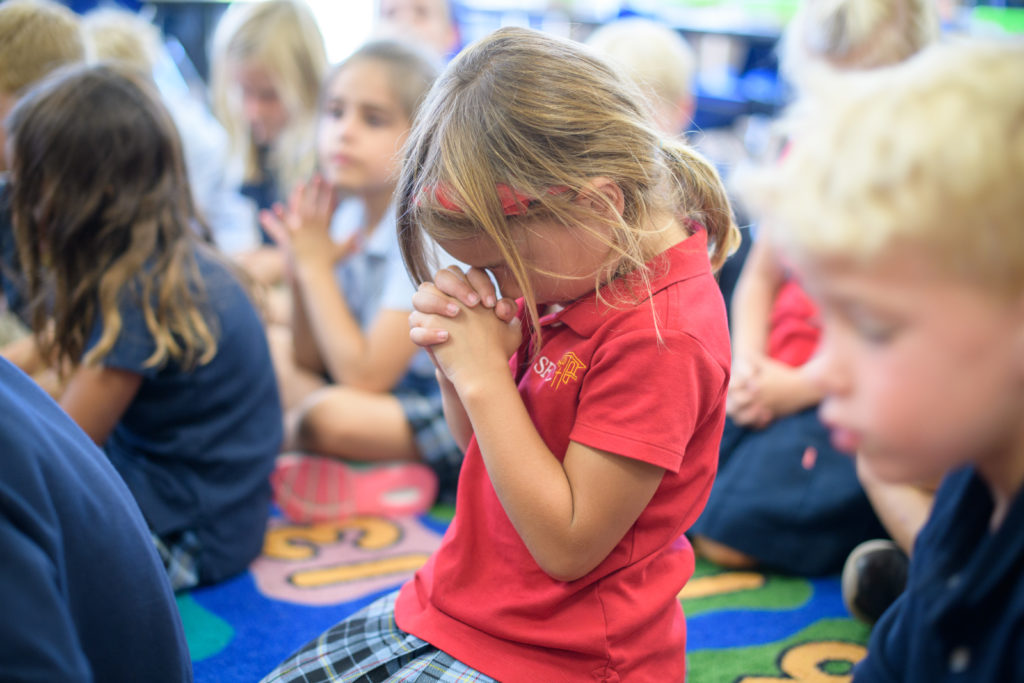 One Santa Fe Christian kindergartener praying with her classmates during carpet time.