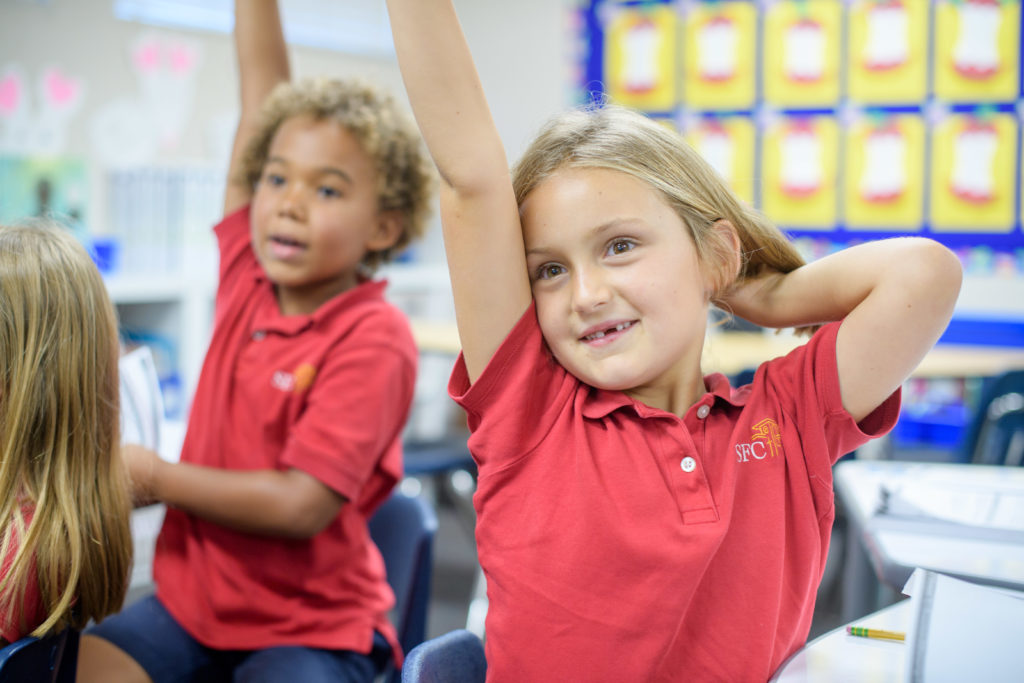 Two Santa Fe Christian kindergarteners raising their hands in class.