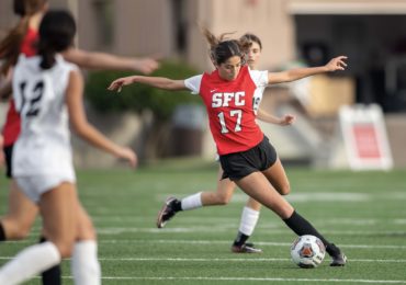 SFC womens soccer player gracefully lines up to punt a ball, mid game.