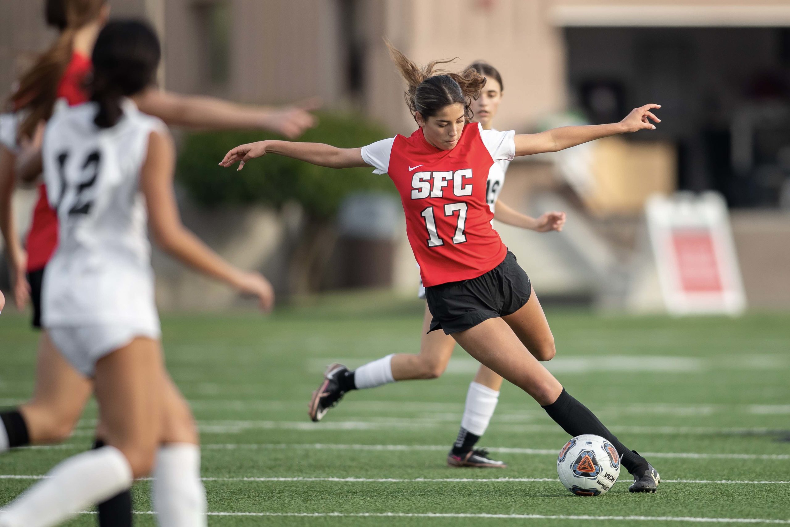 SFC womens soccer player gracefully lines up to punt a ball, mid game.