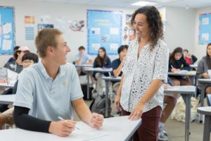 High school math teacher interacts with a student at a desk. 